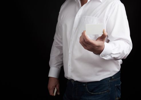 male hand holds a rectangular empty white paper business card,  man dressed in a white shirt, template for a businessman