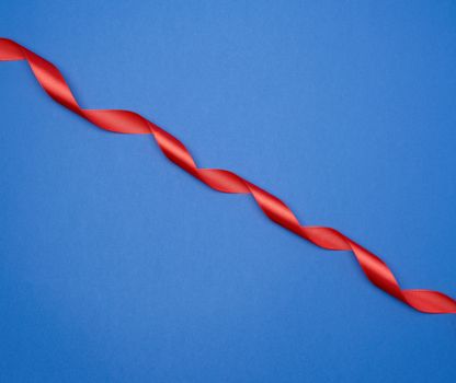 red silk thin ribbon twisted on a blue background, trendy classic color, top view