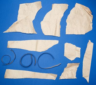 set of various pieces of torn brown crumpled paper on a blue background, close up