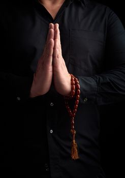 adult man in a black shirt folded his arms in front of his chest in a prayer pose, wearing brown stone rosaries on his hand,  low key