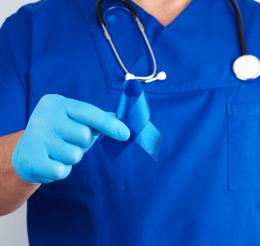 doctor in blue uniform and sterile latex gloves holds a dark blue ribbon, concept of timely research and disease prevention colon malignancies, chronic fatigue syndrome, tuberous sclerosis