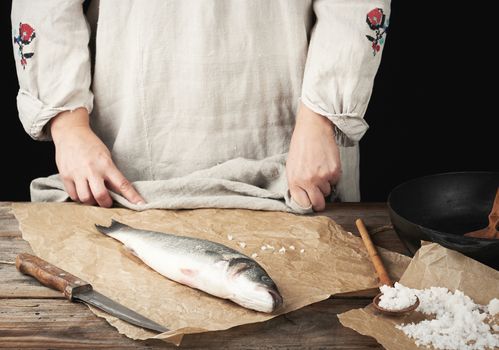 fresh whole sea bass fish lies on the table, cooking process, dark background