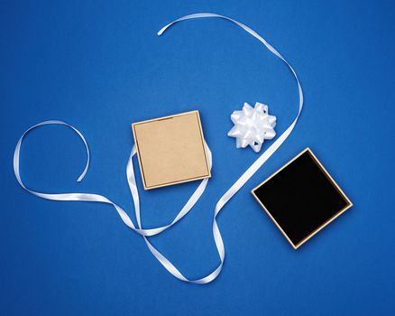 square box with a gift tied with a white ribbon with a bow on a blue classic background, top view, empty place for an inscription