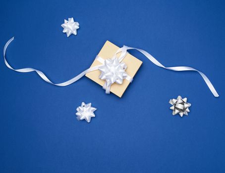closed square box with a gift tied with a white ribbon with a bow on a blue classic background, top view, trend color 
