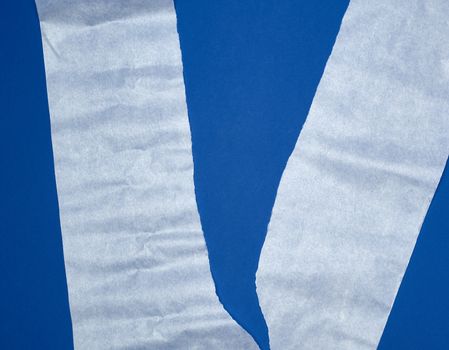 torn piece of white parchment paper on a blue background, close up