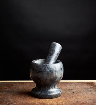 stone mortar with pestle for grinding spices on a brown wooden board, low key
