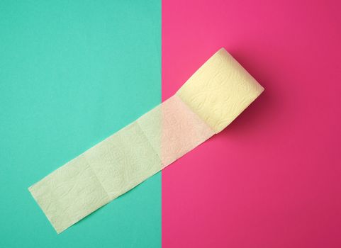 soft yellow toilet paper in a roll on a green-pink background, top view