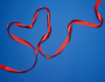 red silk thin ribbon twisted on a blue background, trendy classic color, top view