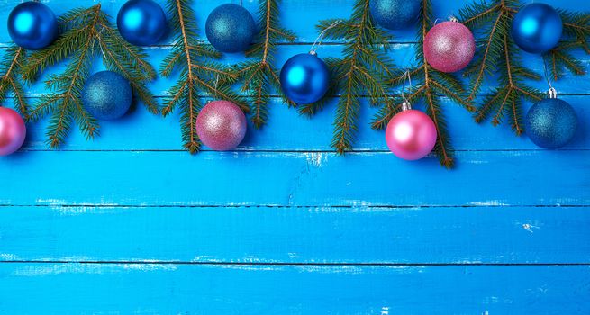 green spruce branches, pink and dark blue shiny Christmas balls on a blue wooden background from boards, festive backdrop for Christmas and New Year,  place for an inscription, Holiday decoration. Winter backdrop