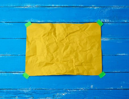 empty yellow crumpled sheet of paper glued with green sticky pieces of paper on a blue wooden background, place for text
