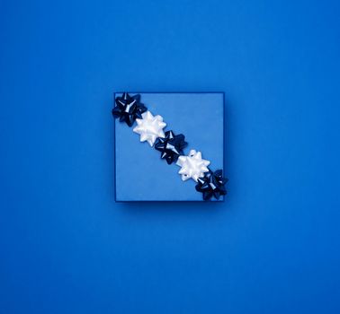 blue square box with a gift with a bow on a blue classic background, top view, empty place for an inscription