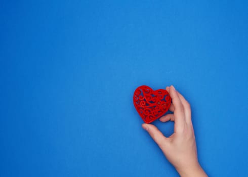 female hand holds a red carved heart on a blue background, place for writing, holiday backdrop