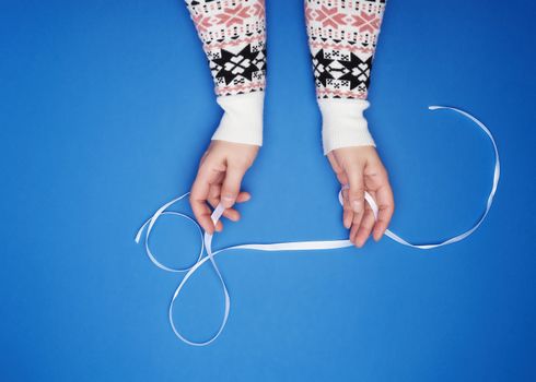 female hands holding a white satin ribbon on a blue background, view of the top