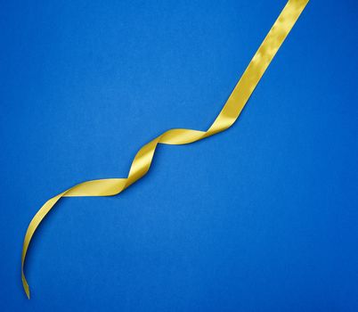 yellow silk thin ribbon twisted on a blue background, trendy classic color, top view