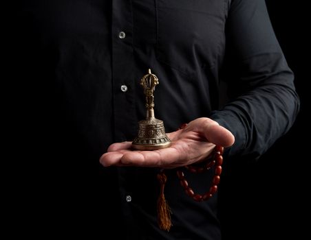adult man in a black shirt holds a copper Tibetan ritual bell, low key. bell represents the feminine principle of excellence in wisdom.