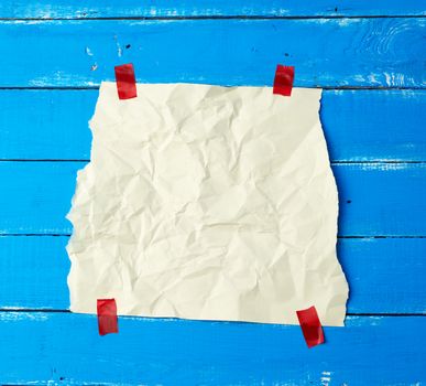 empty white crumpled sheet of paper glued with red sticky pieces of paper on a blue wooden background, place for text