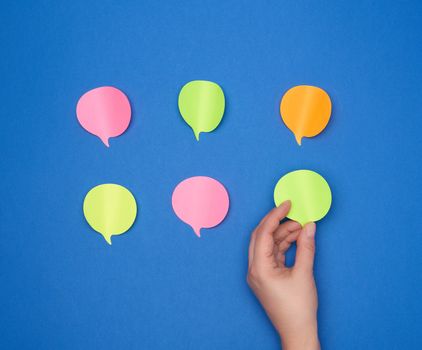 empty paper multi-colored stickers in the shape of a cloud and a female hand glues one piece of paper on a blue background, dialogue concept