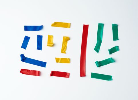 set of torn multicolored rubber pieces of electrical tape glued to a white background, close up