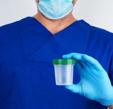 doctor in blue uniform and latex gloves is holding an empty plastic container for taking urine samples, concept of timely diagnosis
