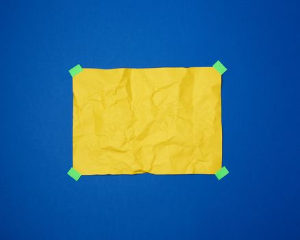 empty yellow crumpled sheet of paper glued with green sticky pieces of paper on a blue background, place for text
