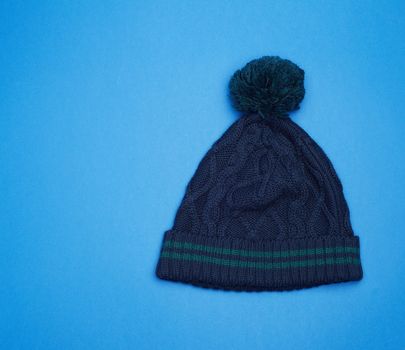 dark blue knitted hat with pompom on a blue background, top view