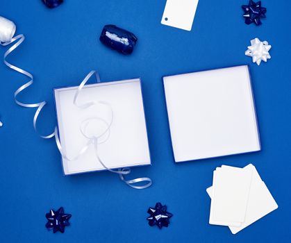 open cardboard gift square boxes, bows, ribbons for packaging on a dark blue background, top view, trend colors