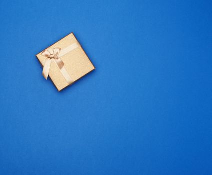golden cardboard gift square box tied with a ribbon on a dark blue background, top view, trend colors, copy space