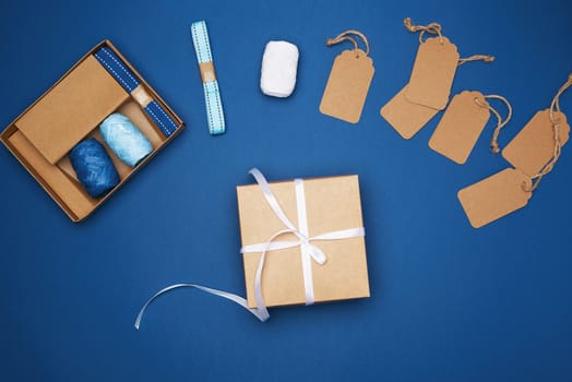 brown cardboard box tied with a white ribbon and a set for packing holiday gifts on a blue background, top view