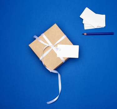 cardboard gift square box tied with a white thin ribbon and white empty card on a dark blue background, top view, trend colors