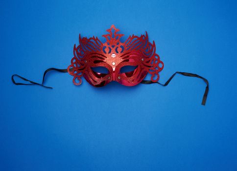 female red carved mask with black ties on a dark blue background, close up