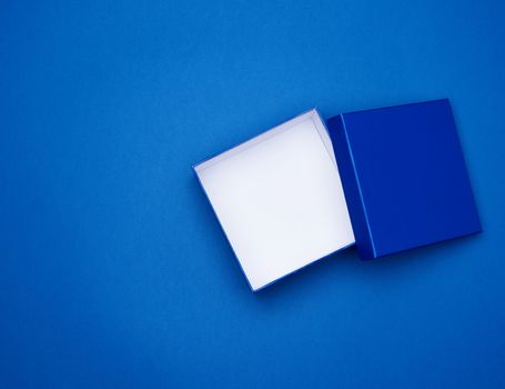 open blue square cardboard empty box, item lies on a blue classic background color, top view