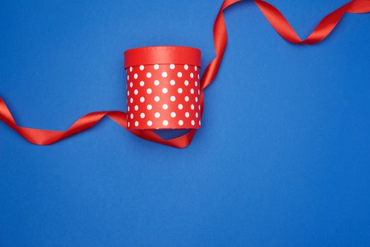 closed cardboard red box with white polka dots and red silk ribbon on a blue background, holiday backdrop