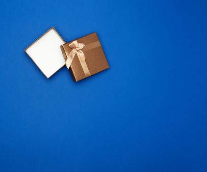open brown square cardboard empty box, item lies on a blue classic background color, top view, copy space