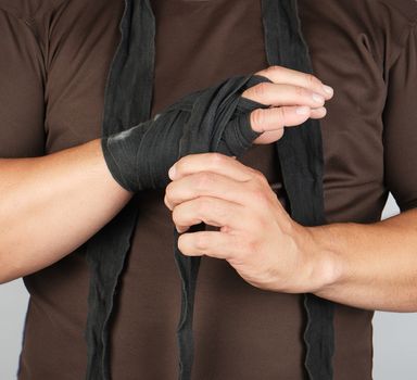 man wraps his hands in black textile bandage for sports, white background, close up