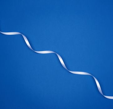 white silk thin ribbon twisted on a blue background, trendy classic color, top view