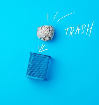 ball of crumpled gray paper and metal blue wastebasket, concept of waste recycling and environmental pollution