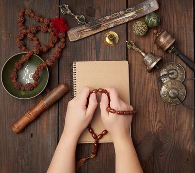 two hands in a prayer pose on a wooden brown table in the middle of vintage Tibetan meditation tools, alternative medicine, top view