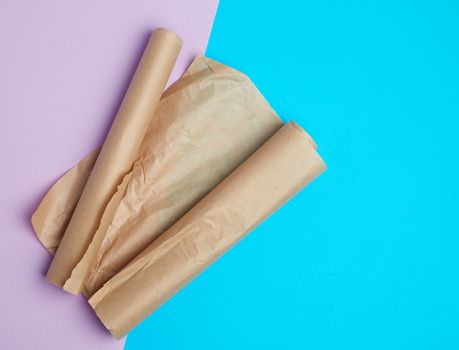 two rolled rolls of brown parchment baking paper on a colored background, top view, place for dough