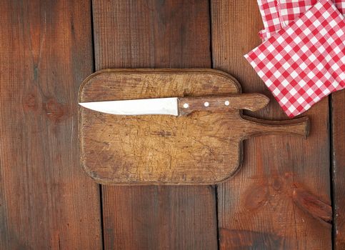very old empty wooden rectangular cutting board and knife, top view, brown wooden background 