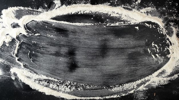 white wheat flour scattered on a black table, inscription frame, top view, culinary background