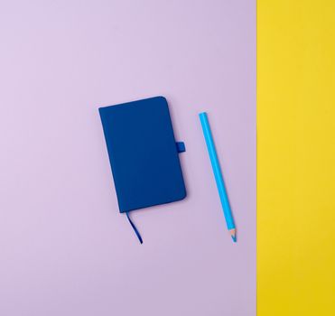 closed notebook and wooden blue pencil on a colored background, top view, flat lay