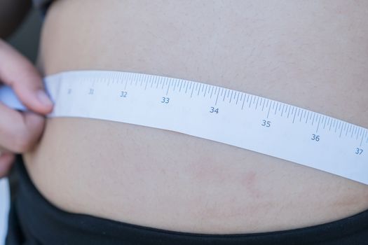 Overweight Fat Asian young woman with tape measuring her belly pinching big in sportswear, overeating problem, obesity. Weight people having more body fat than is optimally, body mass index (BMI)