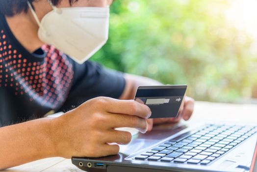 shoping from home in quarantine time/ the man wear mask and holding the credit card for shopping online in website