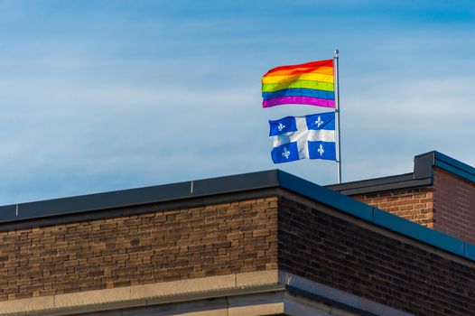 Gay rainbow flag and Quebec flag waving in the wind on the roof of a building in Montreal, Canada