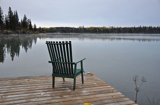 Empty wooden chair on dock on early autumn morning looking out over lake