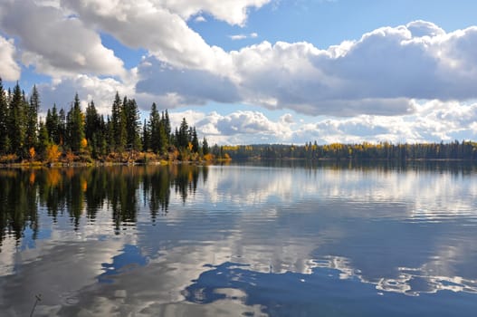 Beautiful autumn forest with clouds reflecting in lake