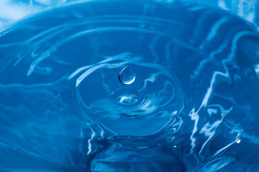 Water drops on blue surface. Water ripple background. Splashes from a drop of water. Raindrops on a blue background. The texture of the water. Aqua, turquoise, macro