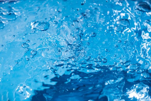 Water drops on blue surface. Water ripple background. Splashes from a drop of water. Raindrops on a blue background. The texture of the water. Aqua, turquoise, macro