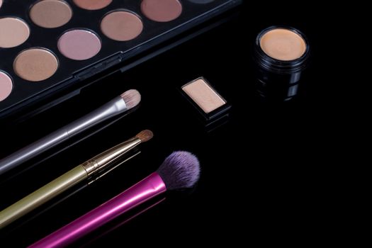 Makeup brushes on black background. Cosmetics, fashion, beauty, glamour. Accessories for make-up artist. Eyeshadow palette, concealer, powder, blush