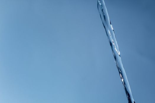 The icy stream of water against a blue background. Cold water, ice water. The glare of light is reflected in the flow of water.